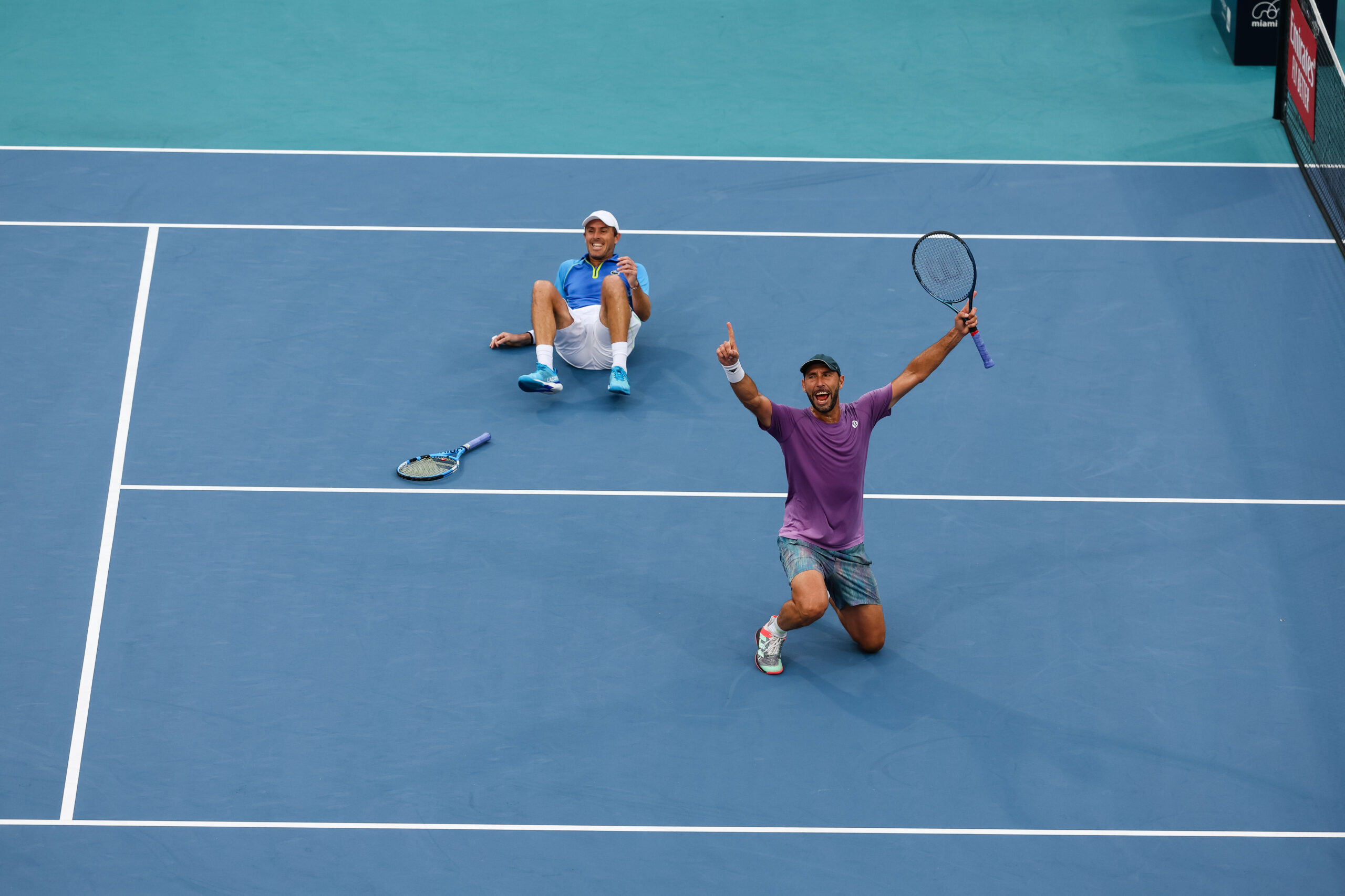 Edouard Roger-Vasselin on the ground while partner Santiago Gonzalez raises his arms after defeating his opponents and reaching the finals of the 2023 Miami Open doubles tournament in Miami Gardens, Florida.