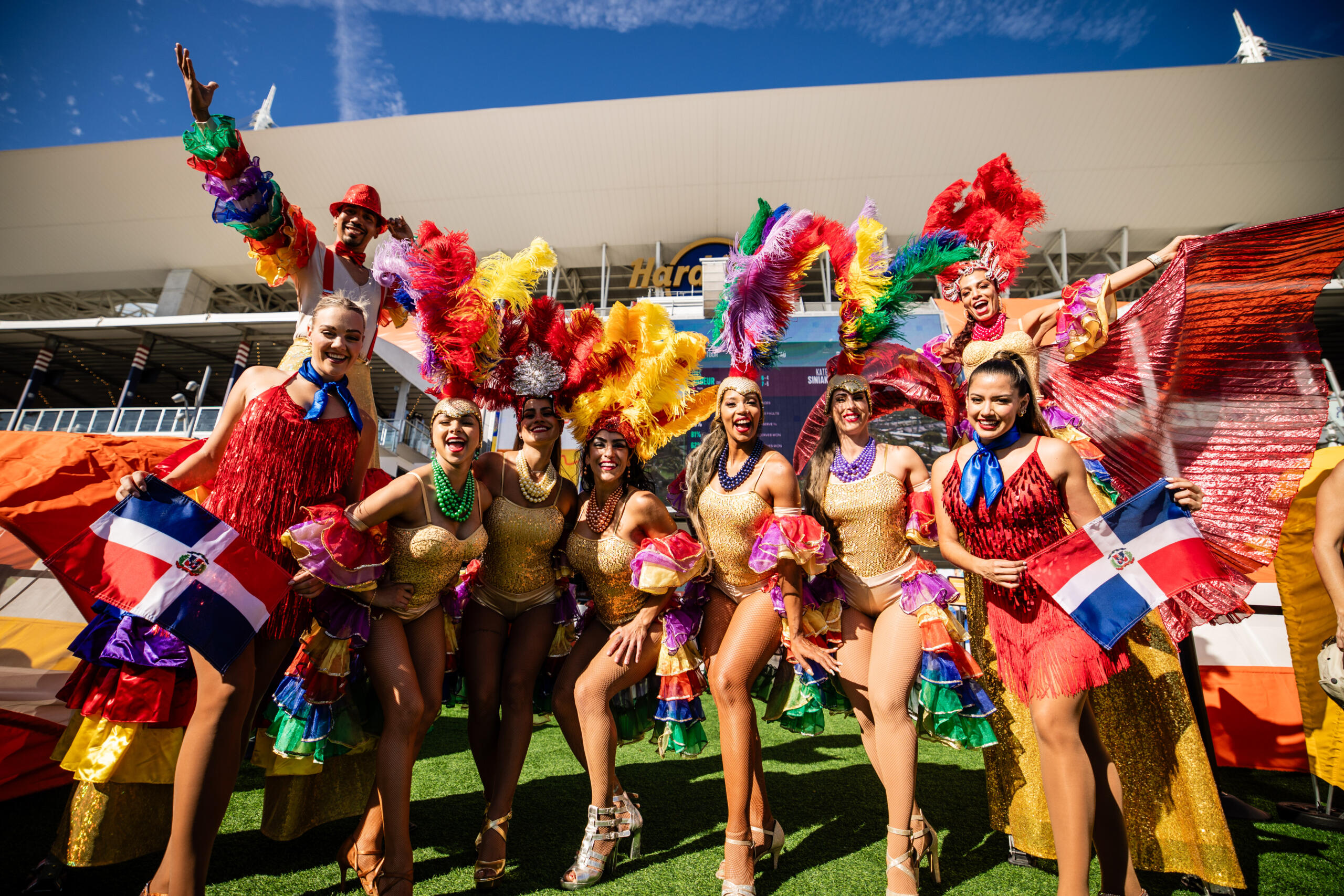 2025 Miami Open A group of dancers in colorful costumes and big feathered head ornaments pose for the picture in front of the hard rock stadium