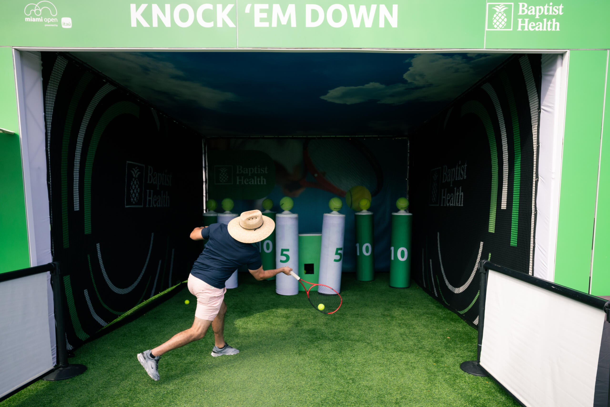 2025 Miami Open Fan in light clothes and a sun hate participates on the Baptist Health Skill Zone trying to knock the big pins with the tennis balls while swingling a tennis racket
