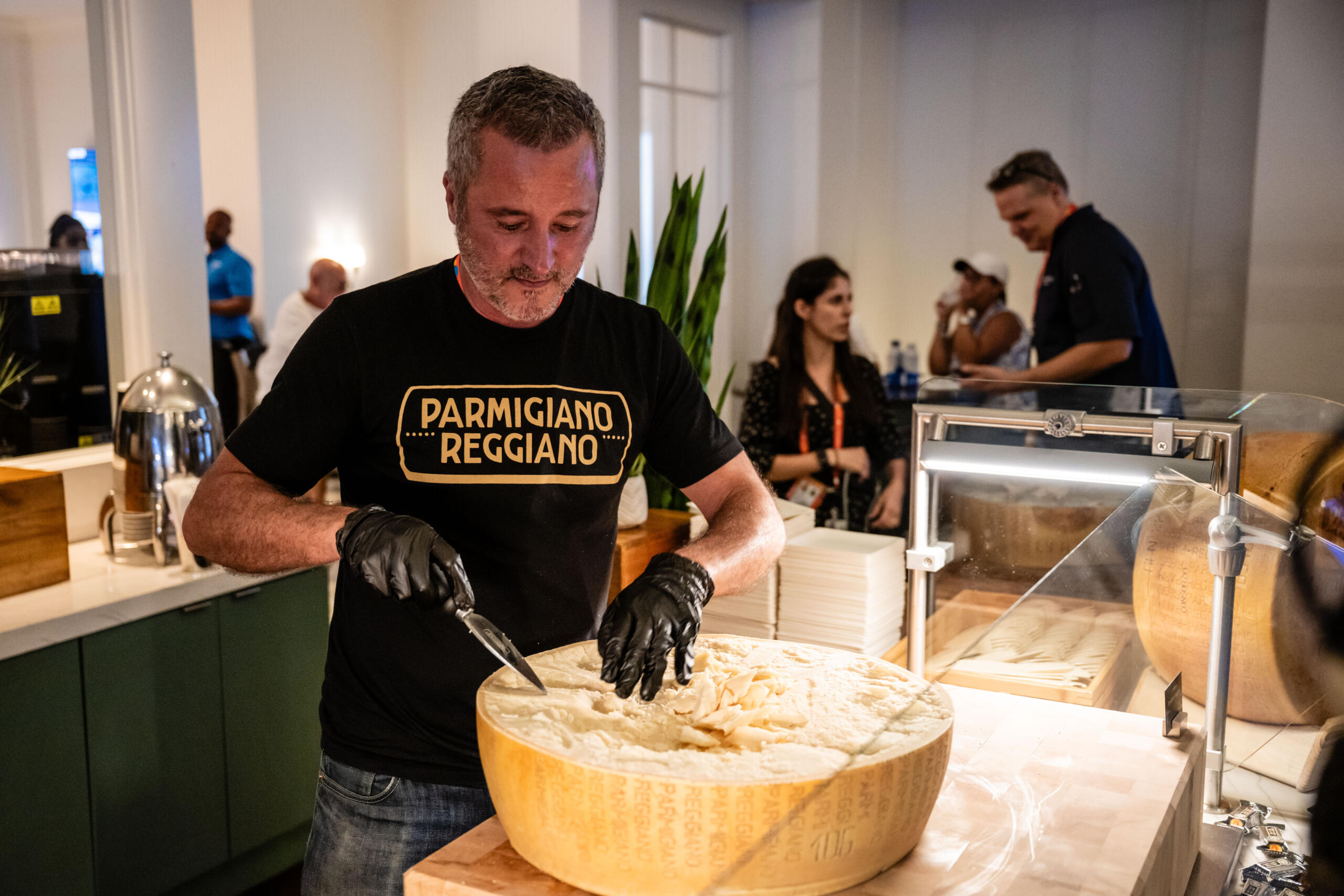 2025 Miami Open Parmigiano Reggiano employee cuts into a bit wheel of cheese