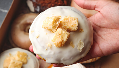 A hand holds up a donut with white icing and toppings