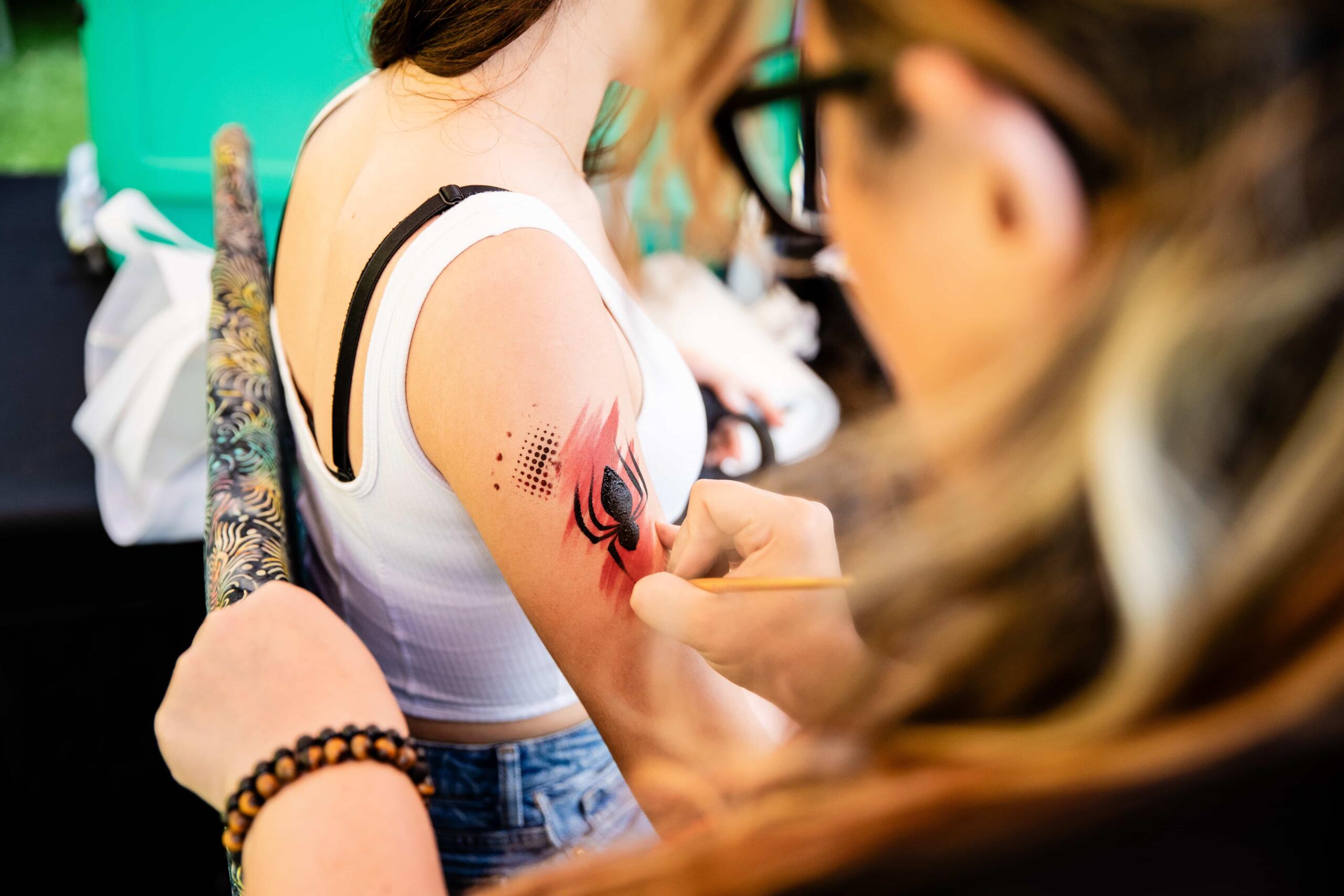 Tattoo artist gives a fan a temporary spider art on the upper arm
