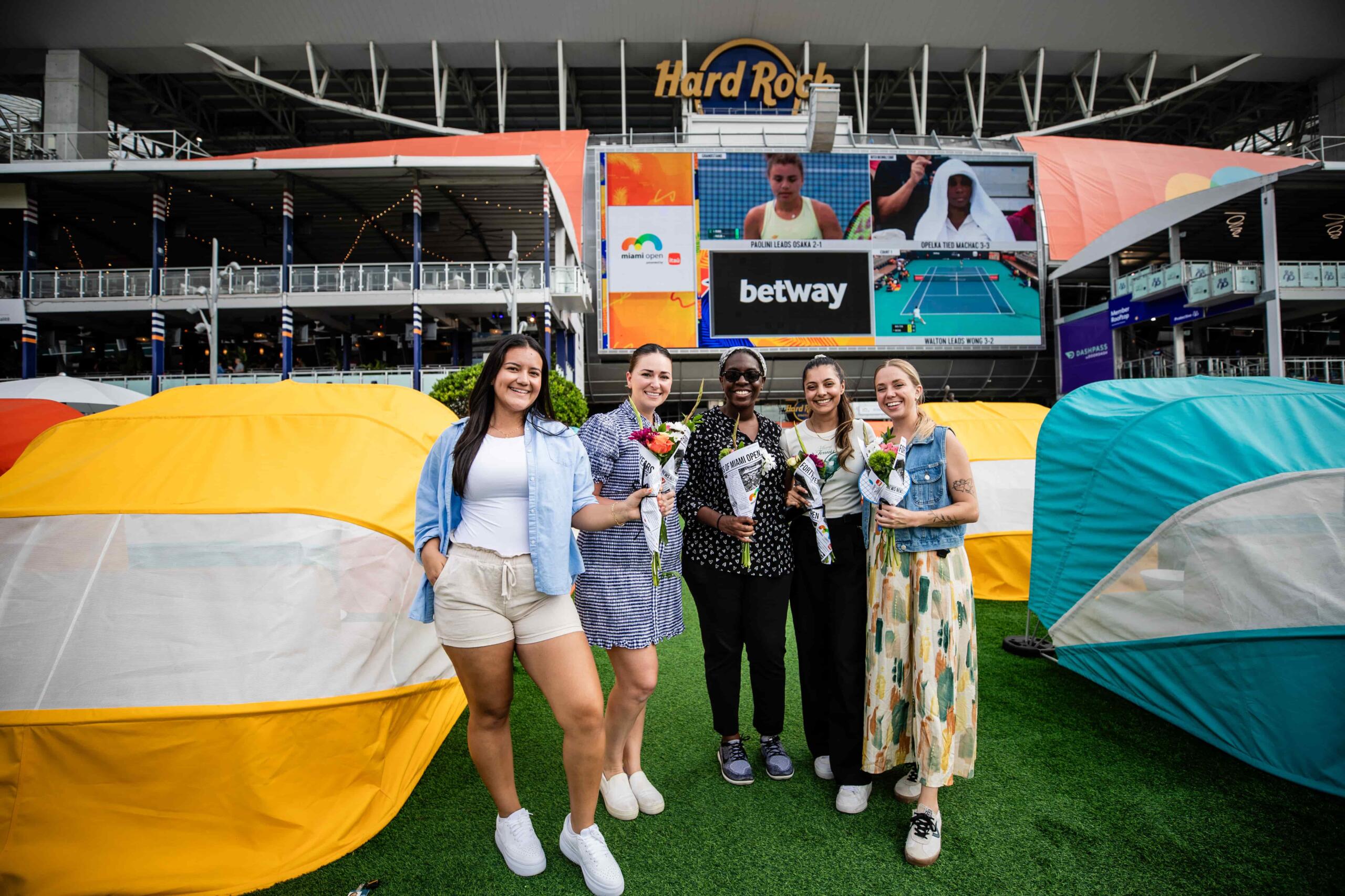 A group of 4 girls posing for picture with their flowers in front of the hard rock stadium