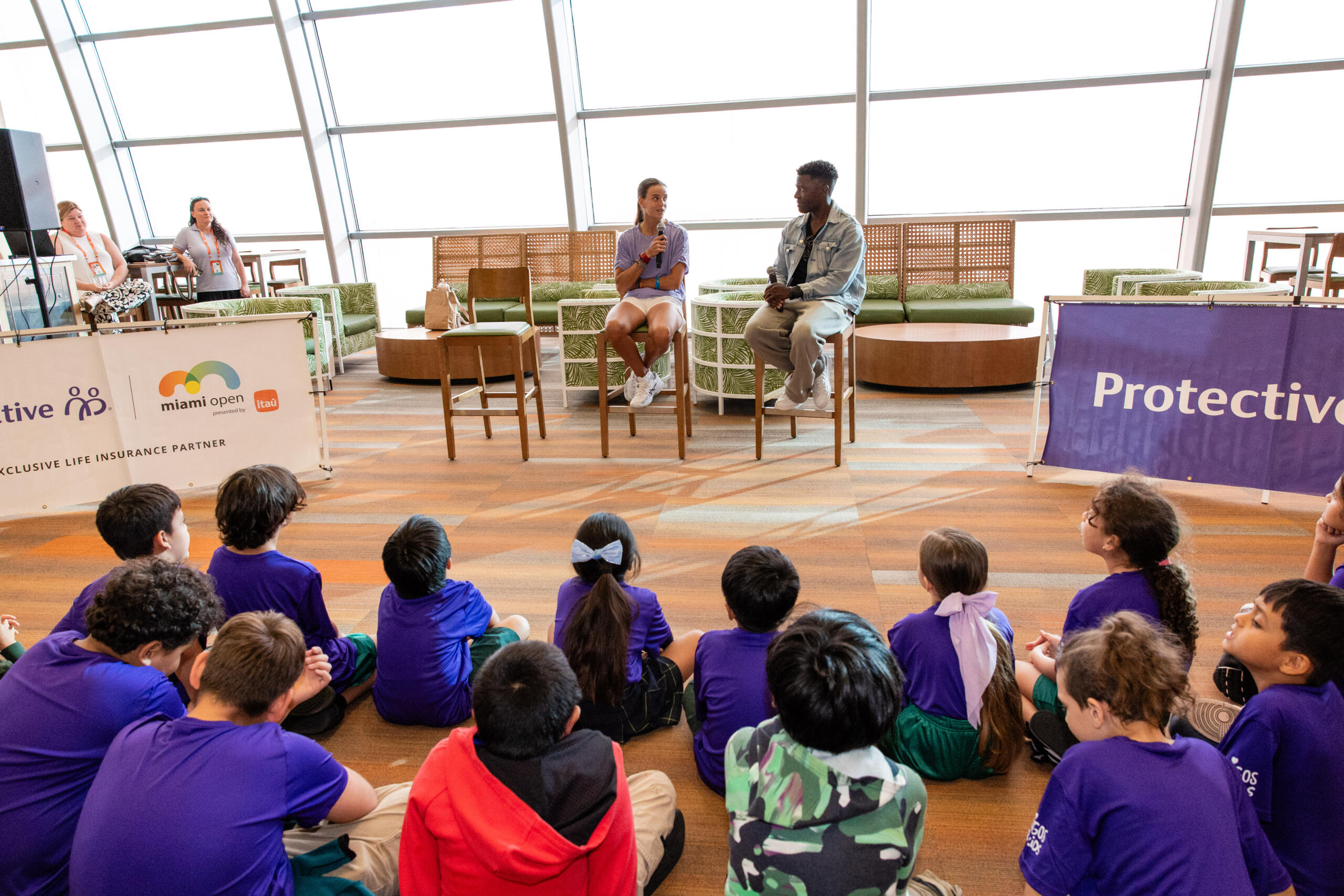 A group of children sits and talks with tennis stars.